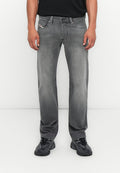 Mann in verwaschenen grauen, geraden Jeans, schwarzen Sneakers und einem schwarzen Shirt, stehend vor einem schlichten weißen Hintergrund.