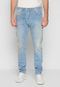 Mann in hellblauen, ausgebleichten Jeans und weißen Sneakers, der vor einem schlichten hellgrauen Hintergrund steht.