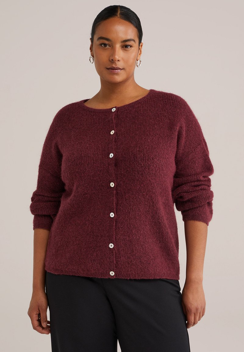 Burgunderfarbene Strickjacke mit lockerer Passform, rundem Halsausschnitt und weißen Knopfverschlüssen an der Vorderseite. Weicher Stoff und umgeschlagene Ärmel.
