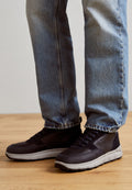Schwarze Turnschuhe mit einem strukturierten Obermaterial aus Leder und einer grauen Gummisohle. Merkmale sind eine Schnürung und ein abgerundetes Design. Kombiniert mit blauen Jeans.