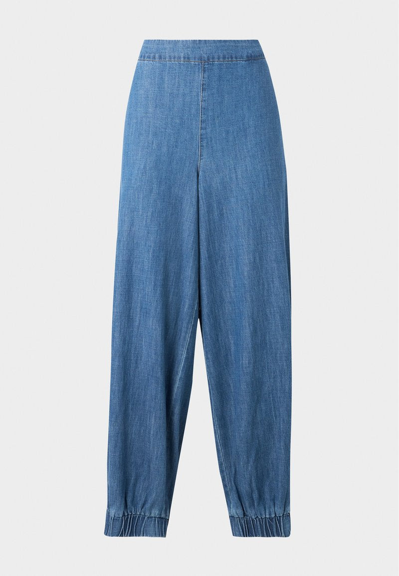 Blaue Denim-Hose mit schmal zulaufendem Bein, elastischen Bündchen und hoher Taille, frontal auf einem einfarbigen hellen Hintergrund gezeigt.