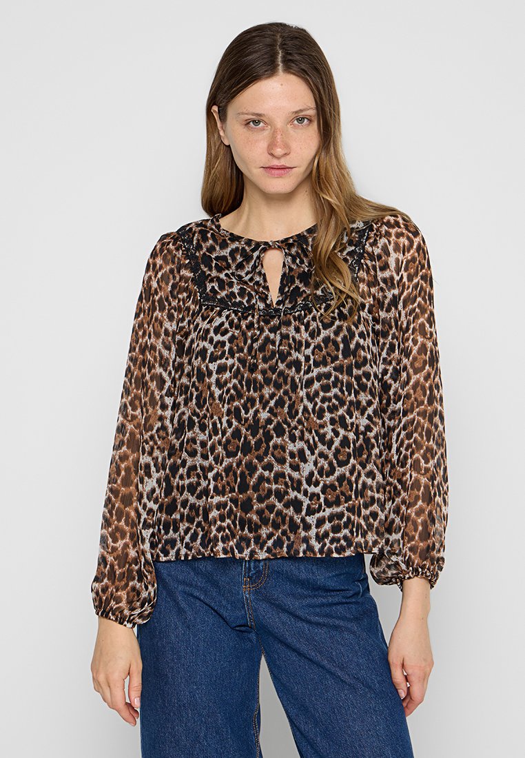 Leopardenmuster Bluse aus durchscheinendem Stoff mit langen Ärmeln, rundem Ausschnitt, Schlüssellochdetail und schwarzen Spitzenakzenten. Kombiniert mit blauen Jeans.