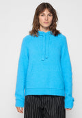 Blauer, flauschiger Hoodie mit einer Vordertasche, verstellbarem Kordelzug, gerippten Bündchen und Saum. Der Stoff wirkt weich und strukturiert.