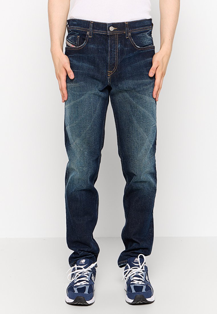 Dunkelblaue Jeans aus Denim mit geradem Bein, verblasster Vorderseite, Fünf-Taschen-Design und kontrastierendem Nähen. Kombiniert mit dunklen Sneakers.