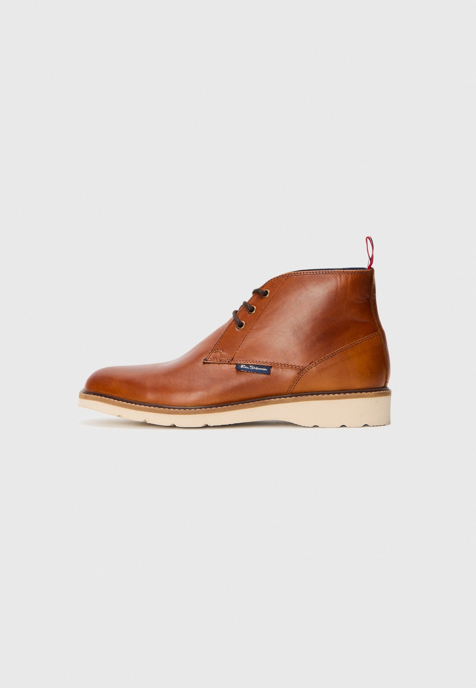 Braune Leder-Stiefeletten mit glatter Textur, runder Zehenpartie und zwei Ösen für Schnürsenkel. Mit einem roten Zugband und einer cremefarbenen Sohle.