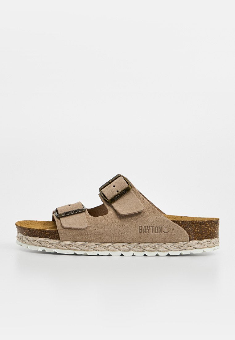 Beiger Wildleder-Sandale zum Hineinschlüpfen mit zwei verstellbaren Riemen mit Schnallen, Kork-Fußbett, weißer strukturierter Sohle und geflochtenem Besatz, seitlich mit der Marke "Bayton" versehen.