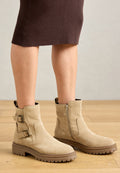 Beige Wildleder Stiefeletten mit zwei seitlichen Schnallen und einem Reißverschluss. Dicke braune Gummisohlen mit geriffelter Textur für besseren Halt.