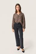 Schwarze und beige gemusterte Bluse mit V-Ausschnitt und Puffärmeln, kombiniert mit hochgeschnittenen schwarzen Jeans und spitzen schwarzen Absatzschuhen.