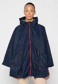 Marineblauer wasserdichter Poncho aus leichtem Material, mit einem Frontreißverschluss in Rotakzenten und zwei Seitentaschen. Kapuzen-Design für zusätzlichen Schutz.