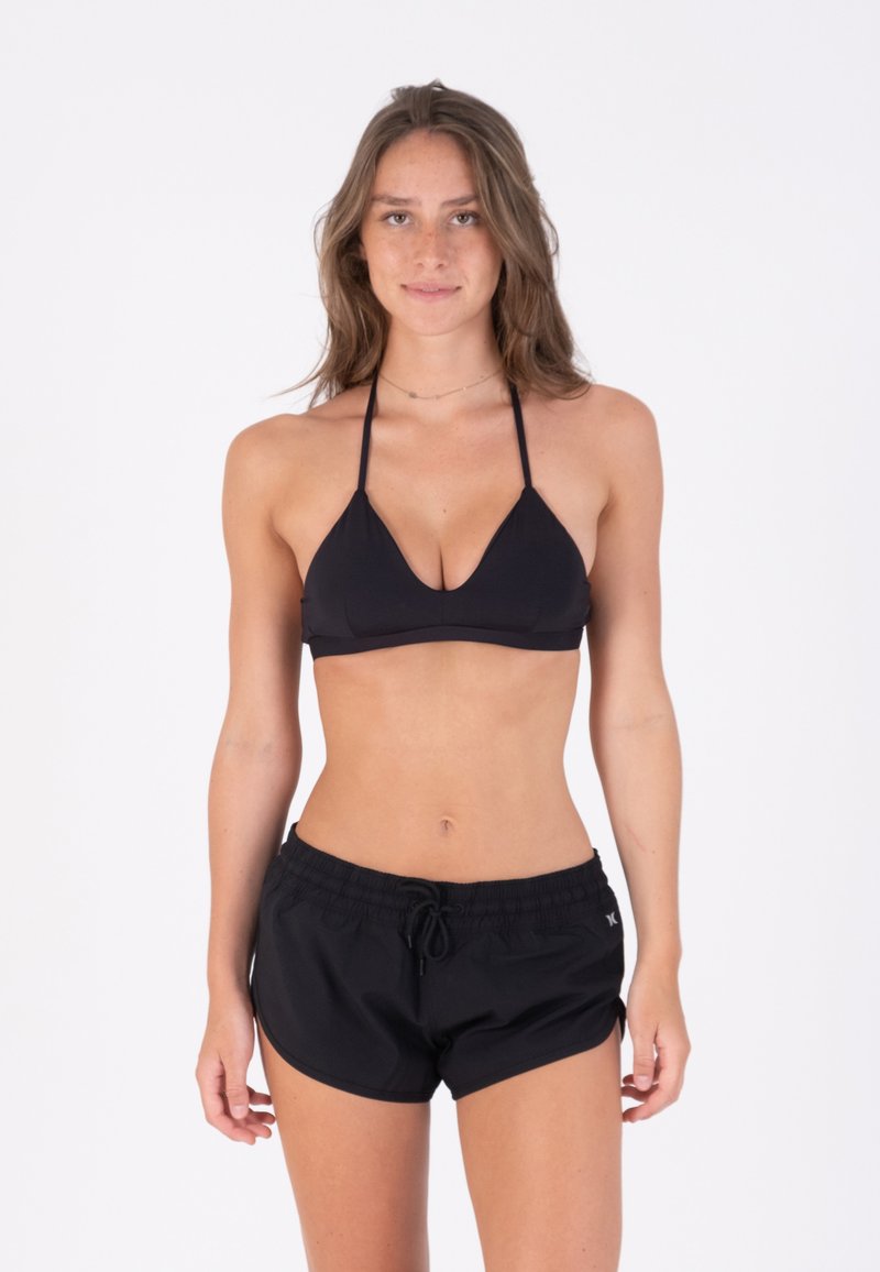 Schwarzer Bikini-Oberteil mit dreieckigen Cups und dünnen Trägern, kombiniert mit schwarzen Shorts mit Kordelzug. Glatte Textur und bequeme Passform.