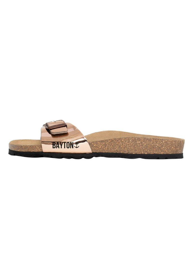 Metallic roségoldene Rutschen-Sandale mit einem breiten Riemen und einer Schnallenakzentuierung, Korkfußbett und schwarzer Gummisohle. Markenname angezeigt.