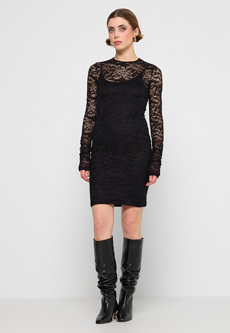 Schwarzes Spitzenkleid mit figurbetonter Silhouette, langen Spitzenärmeln und Rundhalsausschnitt. Kombiniert mit knielangen, schwarzen, lässigen Stiefeln.