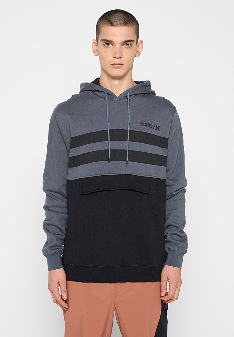 Grau-schwarzer Kapuzenpullover mit einer vorderen Tasche, horizontalem Streifenmuster und einer Kordelzug-Verschluss. Hergestellt aus weichem Stoff.