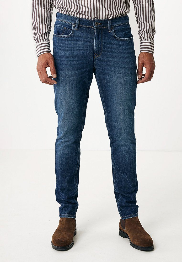 Dunkelblaue Jeans aus Denim mit schlanker Passform, fünf Taschen, dezentem Verblassen und klassischem Design. Kombiniert mit braunen Wildleder-Ankle-Boots.