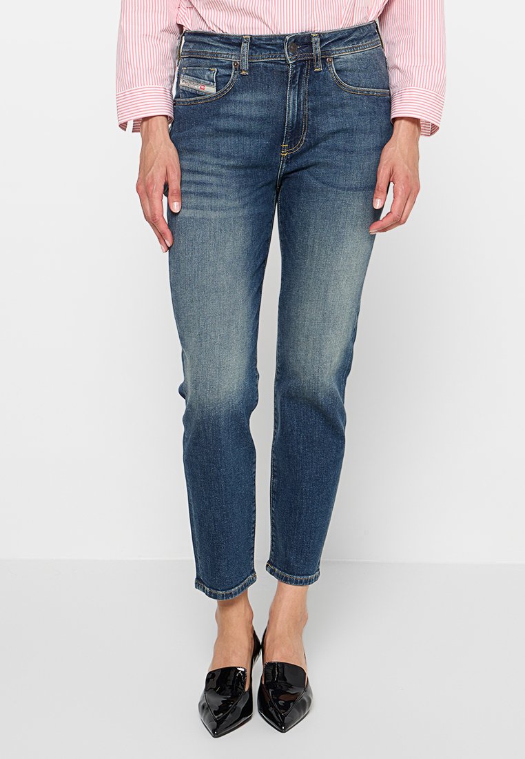 Dunkelblaue Denim-Jeans mit tapered Fit, ausgewaschenen Details, geradem Saum und vorderen Taschen, kombiniert mit schwarzen lackledernen Schuhen.