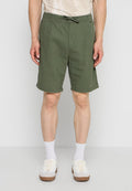 Mann trägt olivgrüne knielange Shorts mit umgeschlagenem Saum, weiße Socken und weiße Sneakers, steht vor einfarbigem Hintergrund.