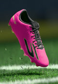 Helle pinke Fußballschuhe mit strukturiertem Obermaterial, schwarzen Akzenten und grünem Outsole. Mit Schnürsenkeln, gepolstertem Kragen und geformten Stollen.