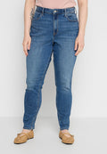 Person trägt blaue Jeans aus Denim und beigefarbene geflochtene Ballerinas, steht mit entspannten Händen an den Seiten vor einem einfarbigen Hintergrund.