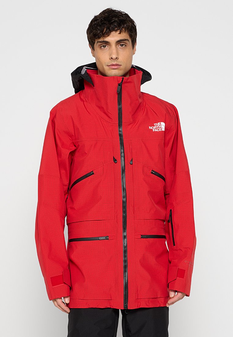 Rote wasserdichte Jacke mit hohem Kragen, mehreren Reißverschlusstaschen und schwarzen Akzenten. Hergestellt aus strukturiertem Material mit Kapuze.