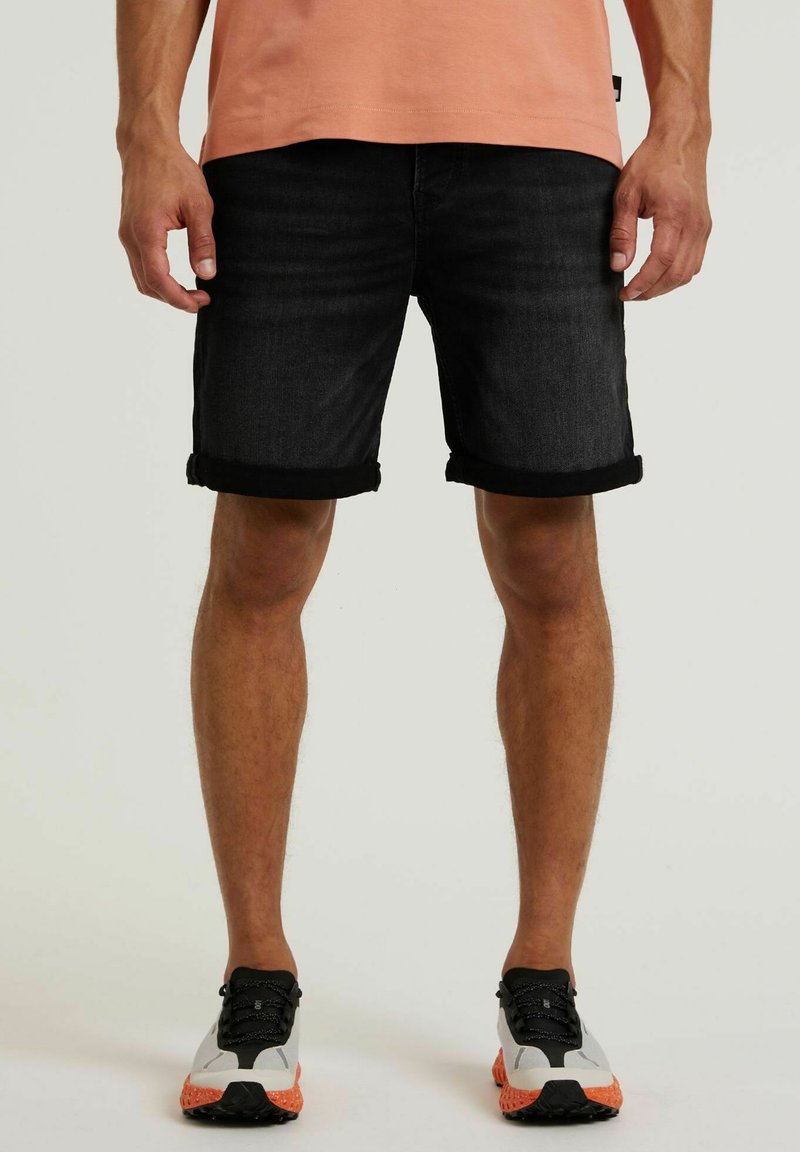 Schwarze Jeansshorts mit umgeschlagenen Säumen, ergänzt durch ein hellpeachfarbenes T-Shirt und mehrfarbige Sportschuhe.