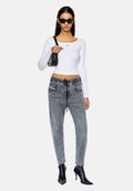 Weißes, geripptes Langarmoberteil mit kleinem rotem Logo, kombiniert mit grauen Denim-ähnlichen Hose mit Zugband und schwarzen, spitzen Absätzen. Schwarze Umhängetasche.
