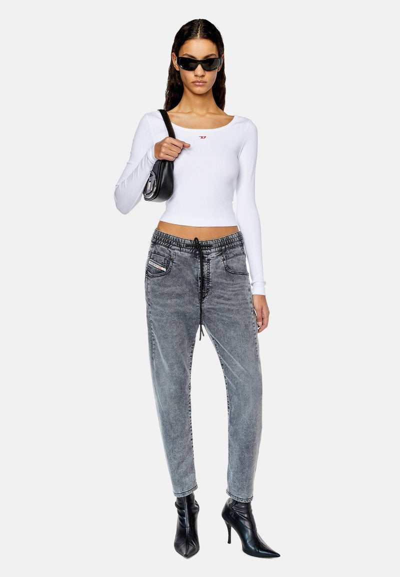 Weißes, geripptes Langarmoberteil mit kleinem rotem Logo, kombiniert mit grauen Denim-ähnlichen Hose mit Zugband und schwarzen, spitzen Absätzen. Schwarze Umhängetasche.