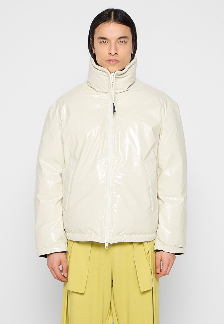 Gefütterte Jacke aus glänzendem cremefarbenem Material, mit hohem Kragen, Frontreißverschluss und seitlichen Taschen. Schlichtes Design mit moderner Silhouette.