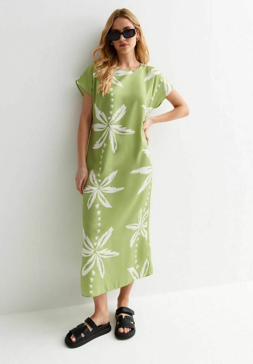 Maxikleid mit grünem Blumenmuster und weißen Blattmotiven; weich fließender Stoff; kurze Ärmel; kombiniert mit schwarzen Sandalen.