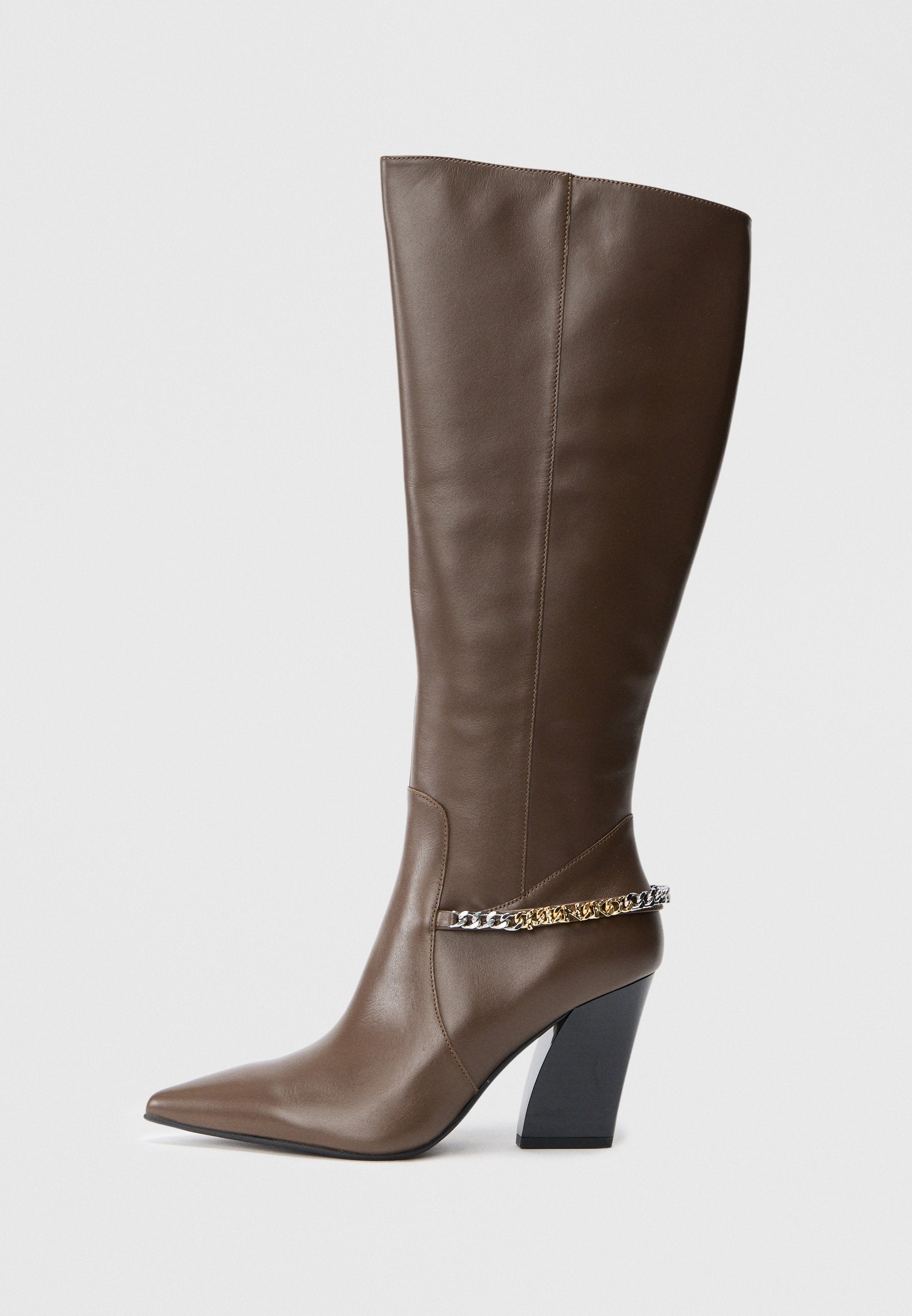 Braune Lederstiefel bis zum Knie mit spitzer Zehe, dicker schwarzer Absatz und metallischer Kettenakzent um den Knöchel. Glatte Textur, minimales Design.