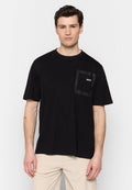 Schwarzes T-Shirt mit kurzen Ärmeln aus Baumwolle, das ein strukturiertes geometrisches Taschendesign auf der linken Brust mit einem kleinen Logo aufweist.