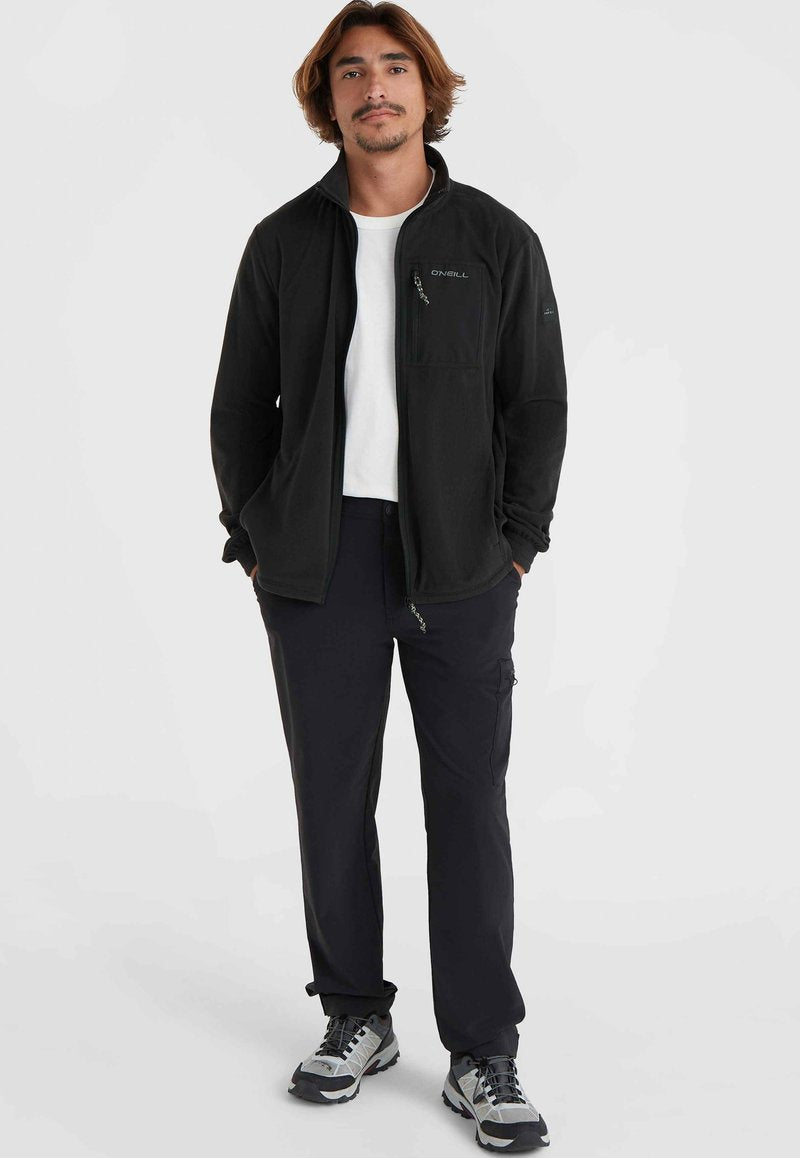 Schwarze Fleecejacke mit Reißverschlusstasche, weißes T-Shirt, dunkle Cargo-Hosen und graue Wanderschuhe. Legere, vielseitige Outdoor-Bekleidung.