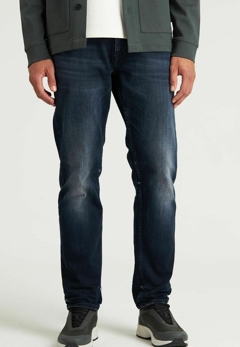 Dunkelblaue Jeans aus Denim mit leichter Ausbleichung, Slim-Fit-Design und klassischem Fünf-Taschen-Stil, kombiniert mit grauen Sportschuhen.
