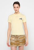 Junge Frau in einem blassgelben kurzärmeligen Shirt mit kleinem Frontlogo und einem beigen Batik-Minirock mit Reißverschluss und Taschen.