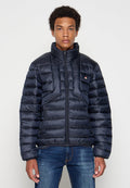 Marineblau gepolsterte Jacke mit hohem Kragen, Reißverschluss und horizontalen Nähten. Verfügt über zwei Seitentaschen und ein kleines Logo auf der Brust.