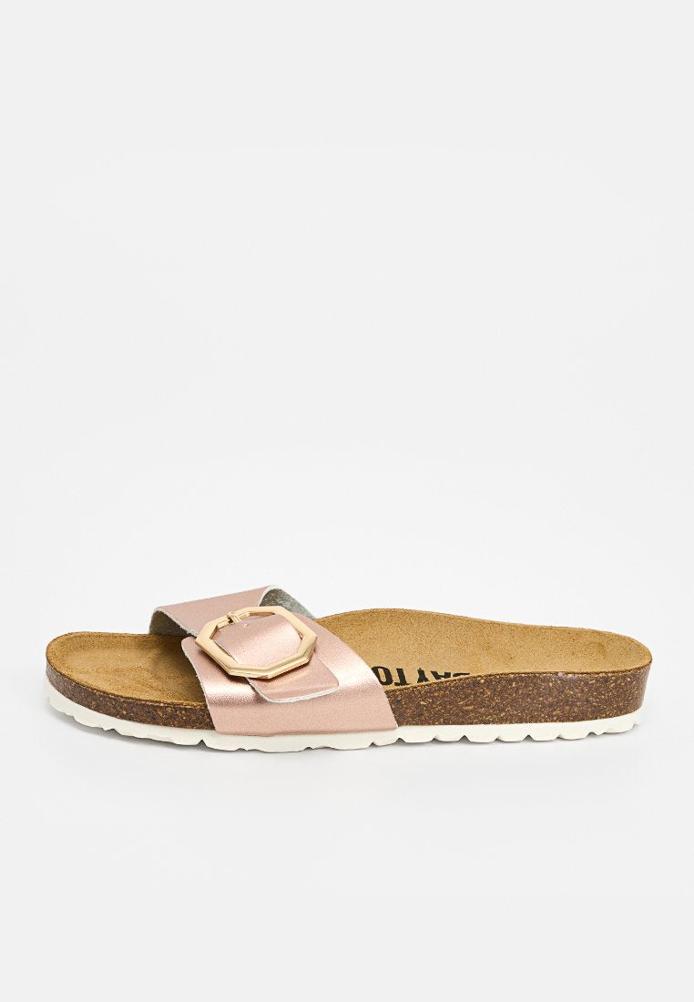 Pantoletten mit Korksohle, weißer strukturierter Außensohle und einem metallic-roségoldfarbenen Riemen mit einer großen geometrischen Schnalle.