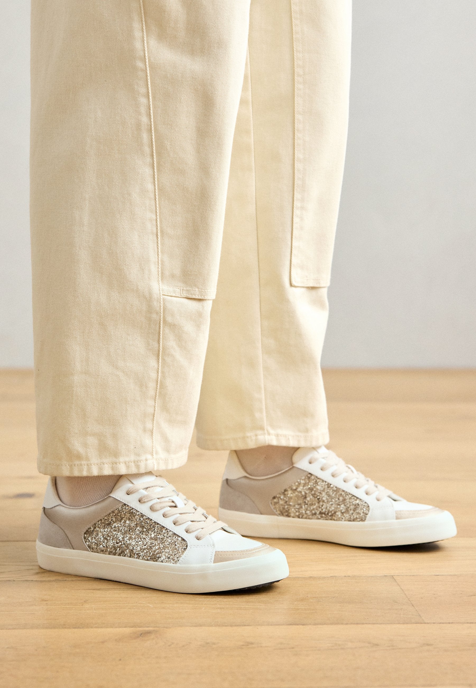 Beige und weiße Sneakers mit einem strukturierten Glitzerpanel an den Seiten, einem glatten Finish und flachen Gummisohlen.