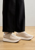 Beige Wildlederschuhe mit einer weißen Plateausohle, ausgestattet mit einer Schnürdesign, geprägtem Logo und strukturierten Akzenten. Kombiniert mit schwarzen Hosen.