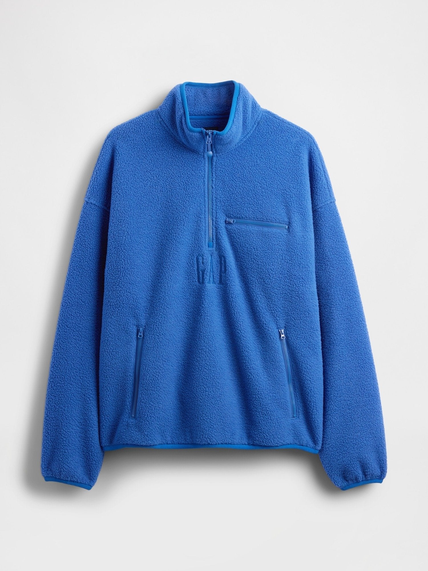 Blauer Fleecepullover mit Reißverschluss bis zur Hälfte, hohem Kragen, Reißverschlusstasche an der Brust und zwei Reißverschlusstaschen an den Händen, mit dezent eingeprägtendem Markenlogo.