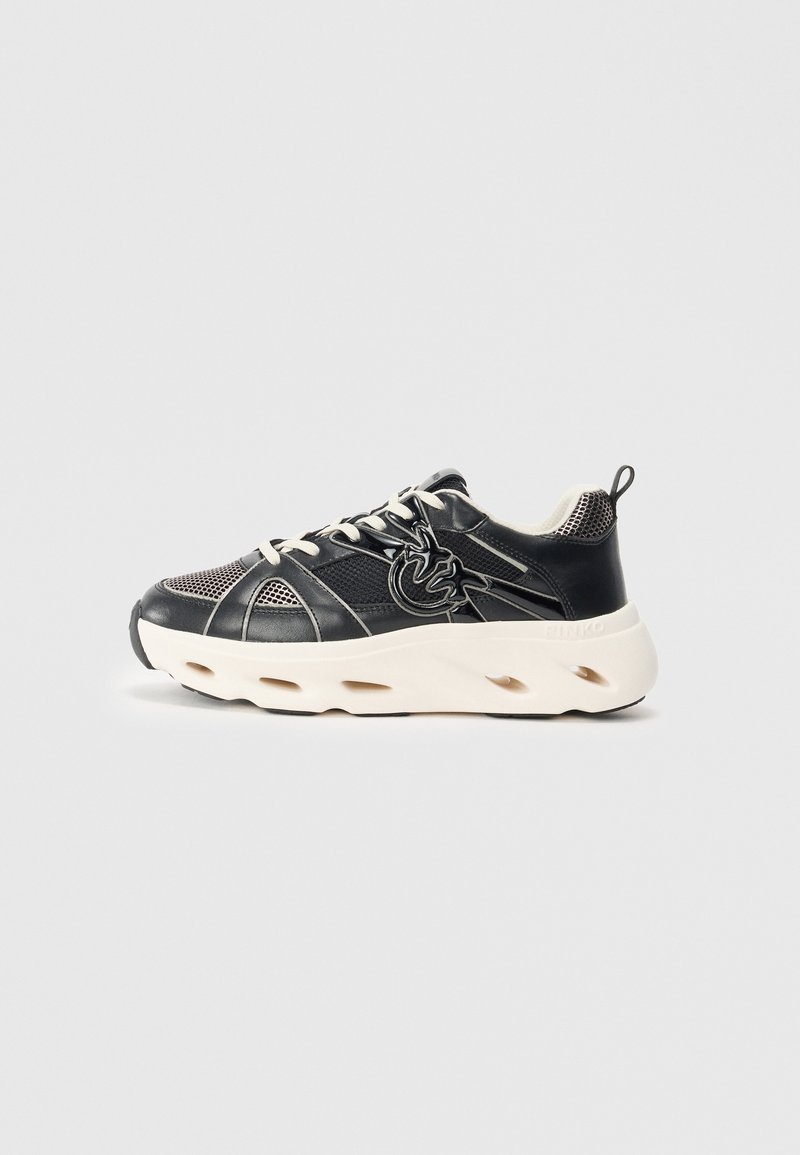 Schwarz-weißer Sneaker aus einer Mischung aus Leder und Mesh-Materialien, mit dicker Sohle und Ausschnitten sowie einem auffälligen Logo-Detail an der Seite.