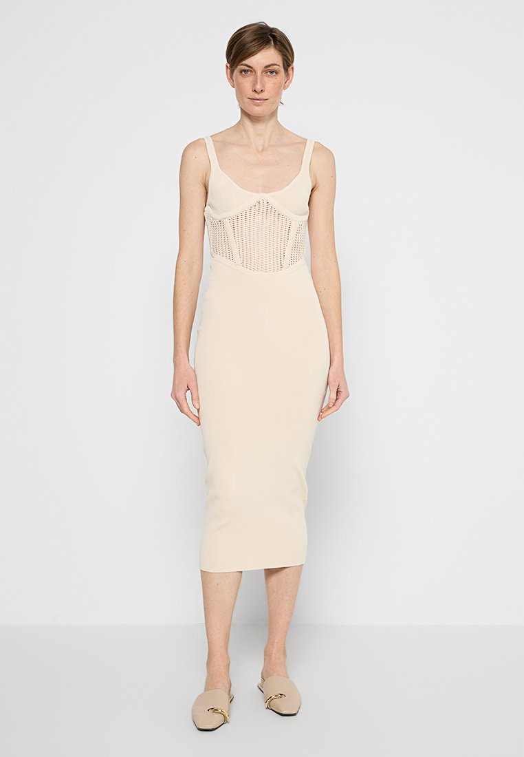 Beige Midi-Kleid mit geripptem Muster, körperbetontem Schnitt, einem strukturierten Mesh-Oberteil und dünnen Trägern. Modell trägt passende beige Slipper.