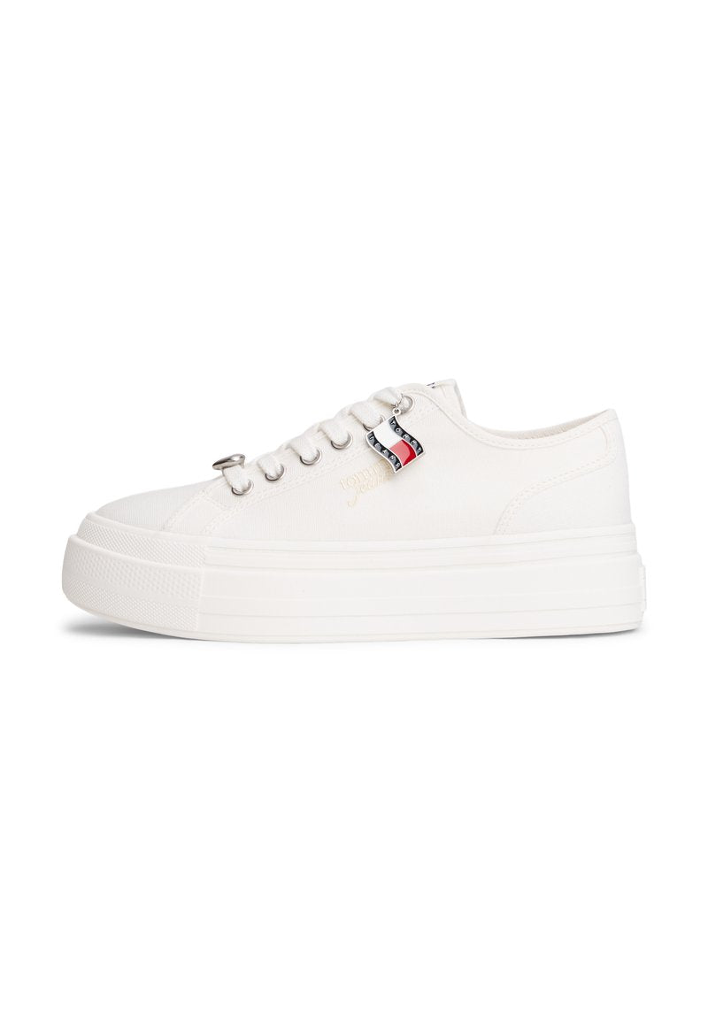 Weißer Plateau-Sneaker mit silbernen Ösen, dicker Sohle und einem kleinen schwarz-weiß-roten Flaggenanhänger nahe den Schnürsenkeln.