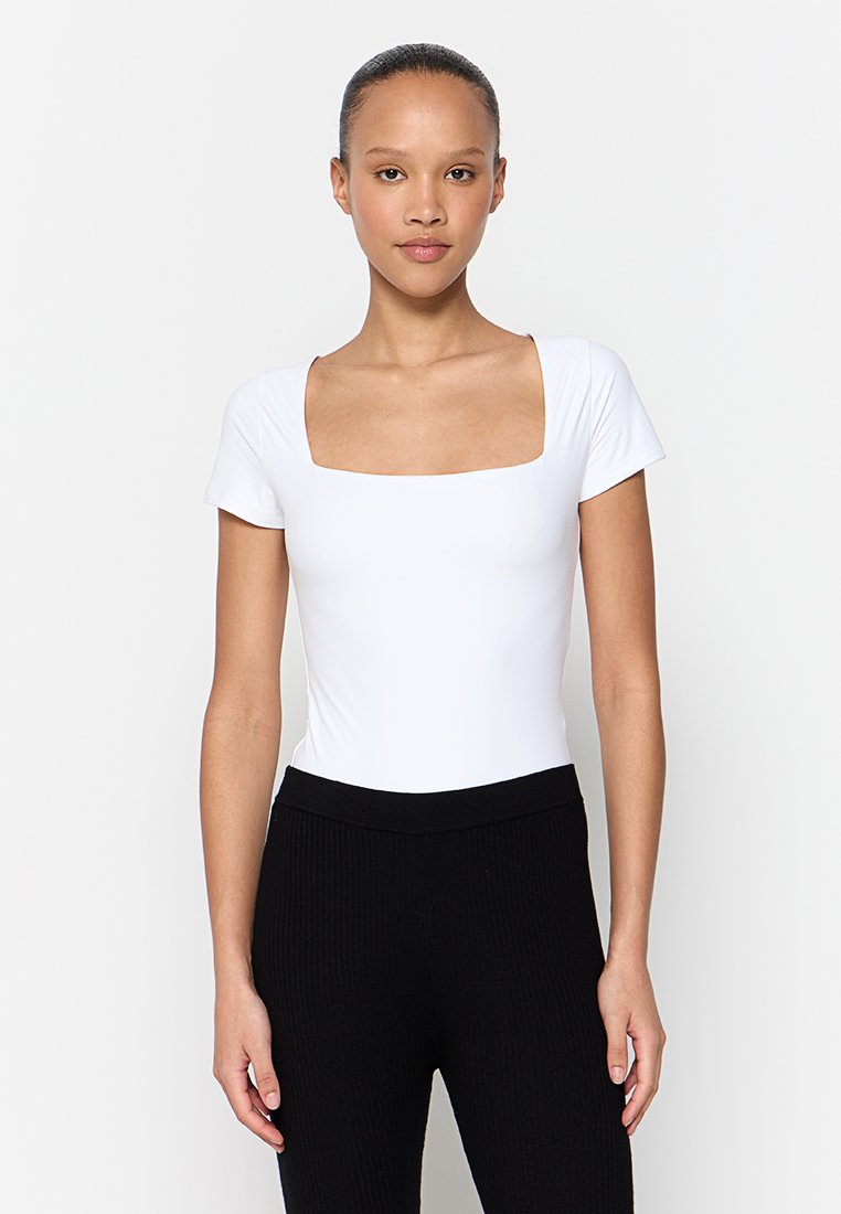 Weißer Kurzarm-Body mit quadratischem Ausschnitt, gefertigt aus glattem Stoff, kombiniert mit schwarzen gerippten High-Waist-Hosen.