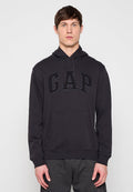 Mann trägt schwarzen GAP-Hoodie mit Fronttasche und Kordelzügen, steht vor hellem einfarbigem Hintergrund.