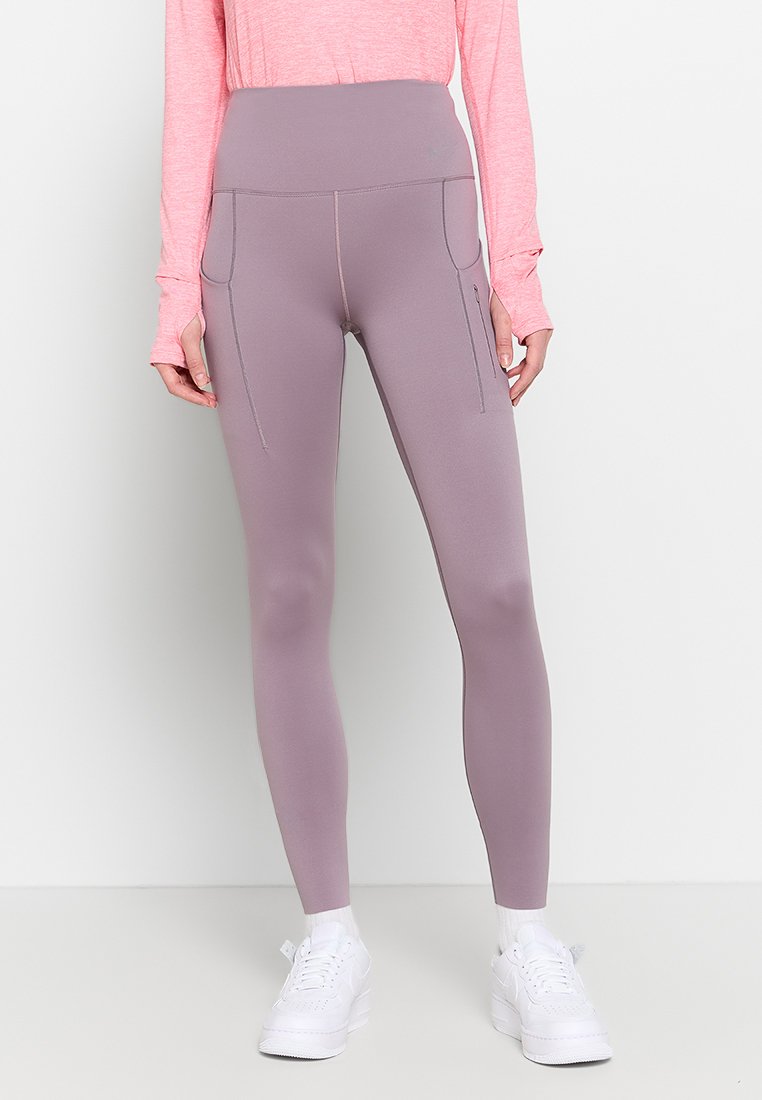 Hochtaillierte, lavendelfarbene Leggings aus dehnbarem Material. Mit Reißverschlusstaschen an den Seiten und einer glatten Textur. Getragen mit weißen Schuhen.