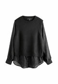 Schwarzer ärmelloser Strickpullover, der über einer transparenten schwarzen Bluse mit gepunkteter Textur getragen wird. Die Bluse hat lange, geknöpfte Ärmel.