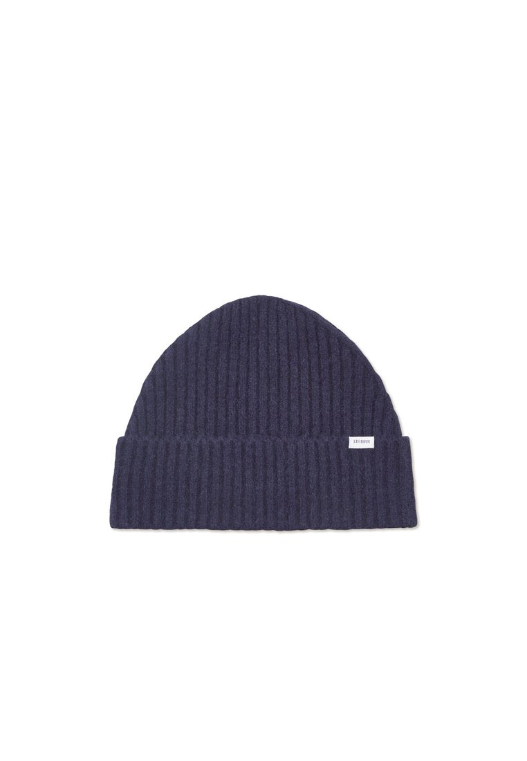 Marineblaues, geripptes Strickmütze mit umgeschlagenem Bund und kleinem Markenlabel an der Seite. Weiche Textur, zylindrische Form und vielseitig für kaltes Wetter.