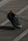 Schwarzer und grauer Outdoorschuh mit einem Netz-Obermaterial, roten Akzenten, reflektierenden Schnürsenkeln und einer dicken Sohle, entworfen für Langlebigkeit und Traktion.