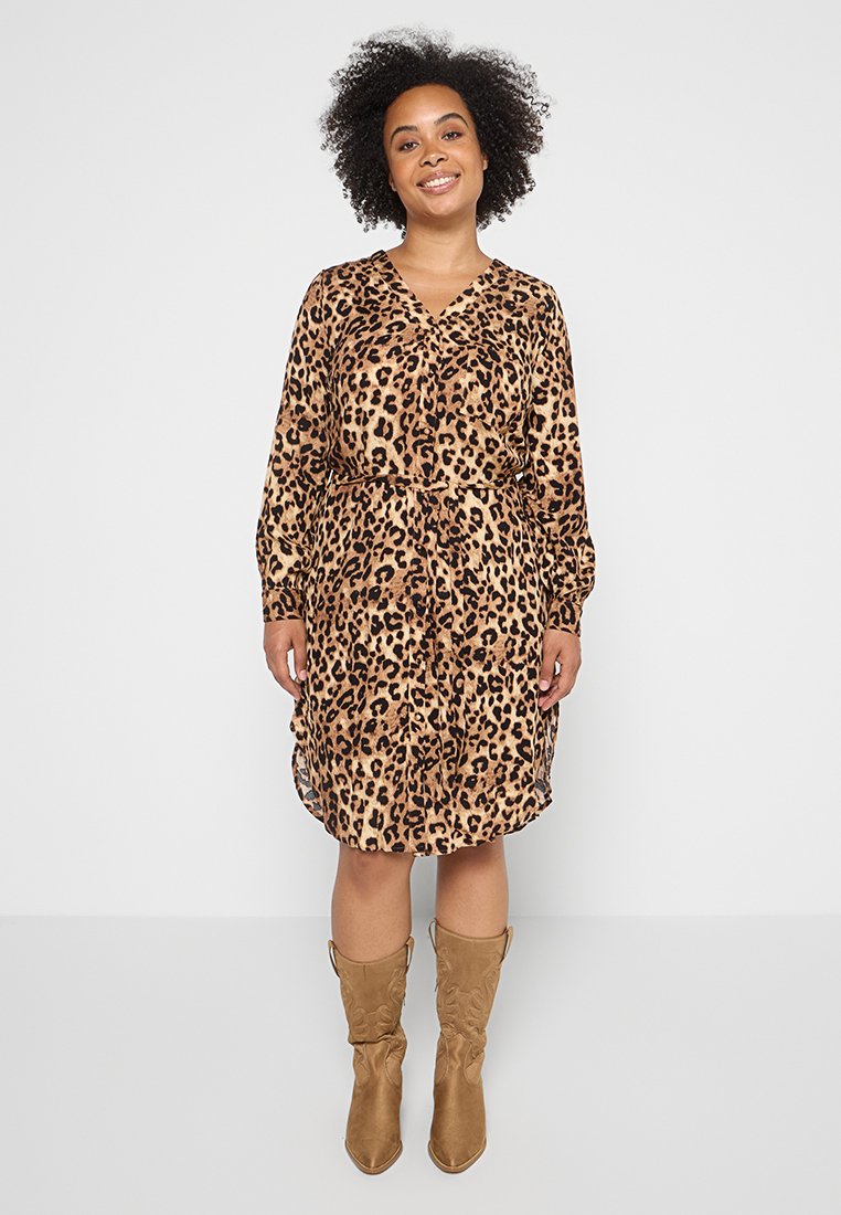 Leopardenmuster-Kleid mit V-Ausschnitt, langen Ärmeln, taillierter Taille und fließender Silhouette, kombiniert mit kniehohen, sandfarbenen Stiefeln.