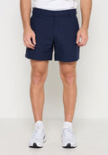 Mann trägt marineblaue, maßgeschneiderte Shorts, weiße Sportsocken und weiße Sportschuhe und steht vor einem schlichten hellen Hintergrund.