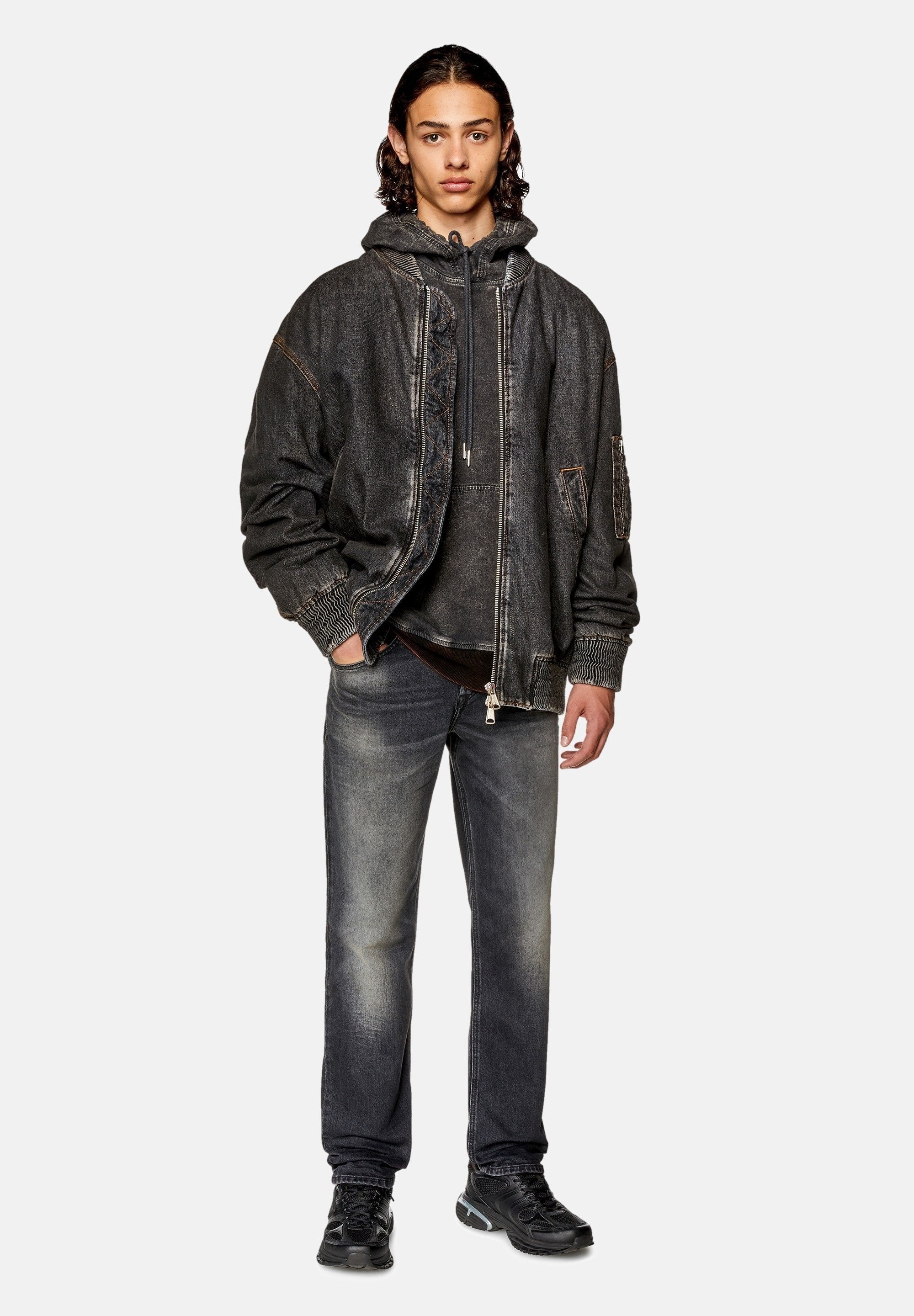 Dunkelgraue Jeansjacke mit sichtbaren Nähten, über einem grauen Hoodie getragen. Kombiniert mit hellgrauen Jeans und schwarzen Sneakers.
